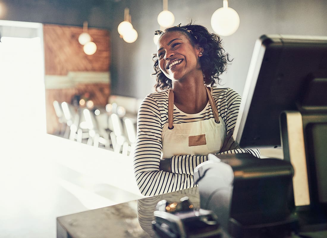 Business Insurance - Portrait of a Cheerful Smal Restaurant Owner Standing in Front of the Cashier Register with her Arms Folded