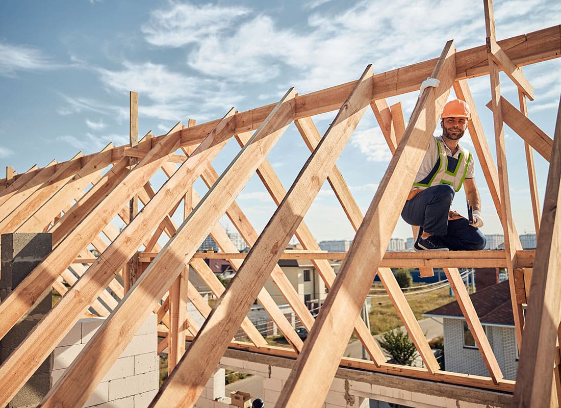 Insurance by Industry - View of a Young Male Contractor Standing on Wooden Beams on a New Roof for a Home Being Built