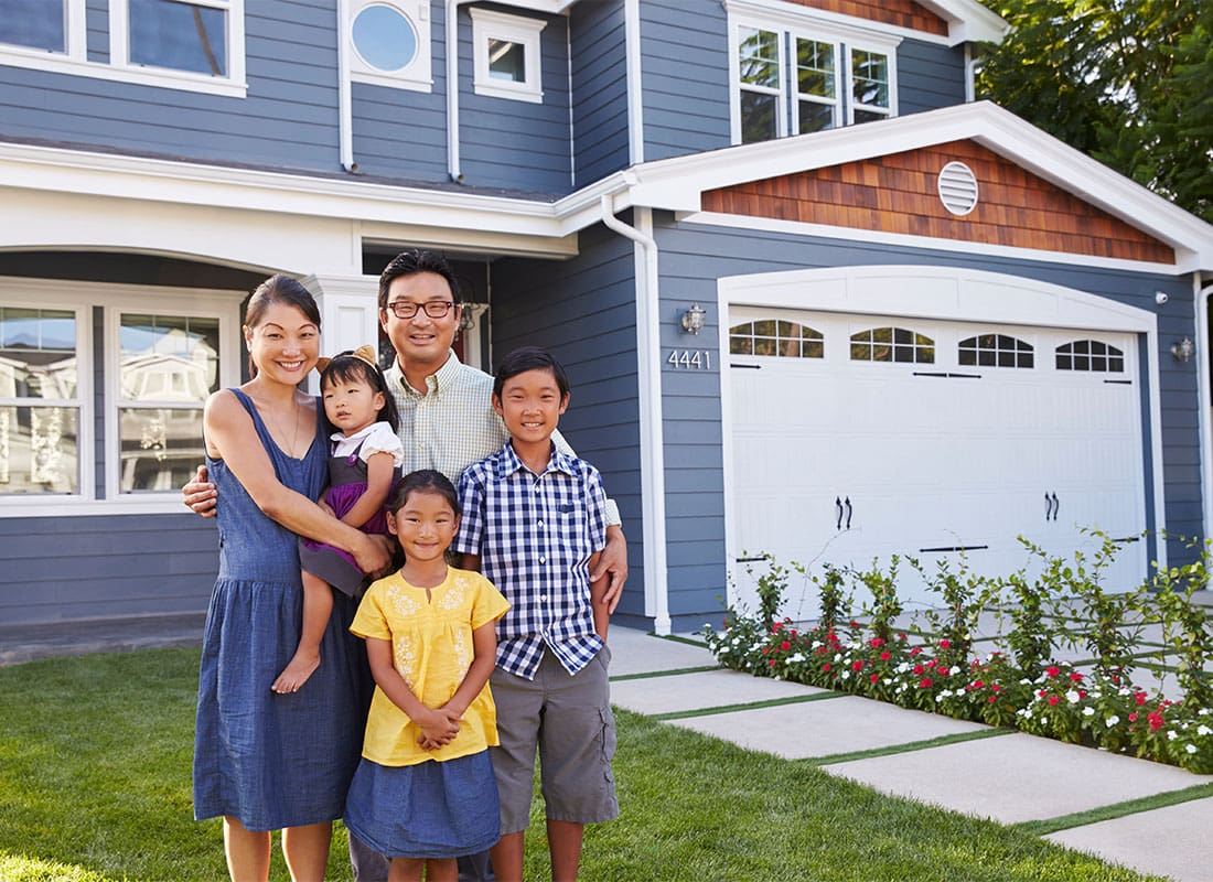 Personal Insurance - Portrait of a Cheerful Asian Family with Three Children Standing in Front of Their Two Story Home on a Sunny Day