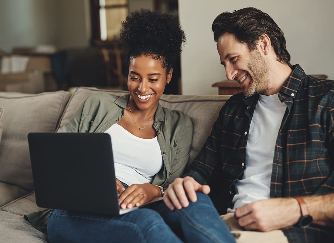 Resources - Cheerful Diverse Married Couple Sitting on the Sofa in the Living Room While Using a Laptop